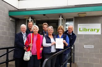 Fakenham Community Archive committee members Alan Leventhall, Howard Young, Anna Coburn, Mo Bruce, Lyn Maple, Chris Chalk and Peter Boggis, show off their CAHG Sustained Achievement award certificate outside Fakenham library.