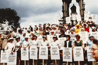 Members of the Women's Institute holding placards naming current and past campaigns, 1980s.