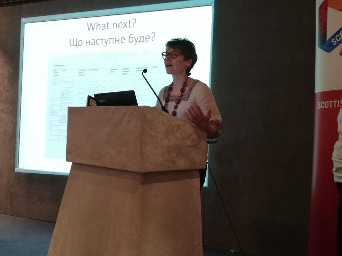 Dr Alexandra Mitchell at the CAHG 2019 Conference. Dr Alexandra Mitchell at the CAHG 2019 Conference.. A person stands behind a lectern gesticulating, a powerpoint is behind them.
