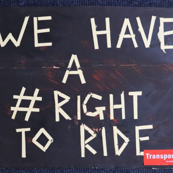 A black cardboard placard. White writing has been made with tape, and says “we have a #right to ride”. In the corner is a red Transport for All logo. | Image courtesy of Transport For All