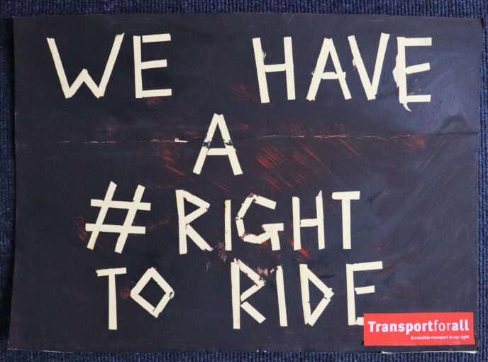 A black cardboard placard. White writing has been made with tape, and says “we have a #right to ride”. In the corner is a red Transport for All logo. | Image courtesy of Transport For All
